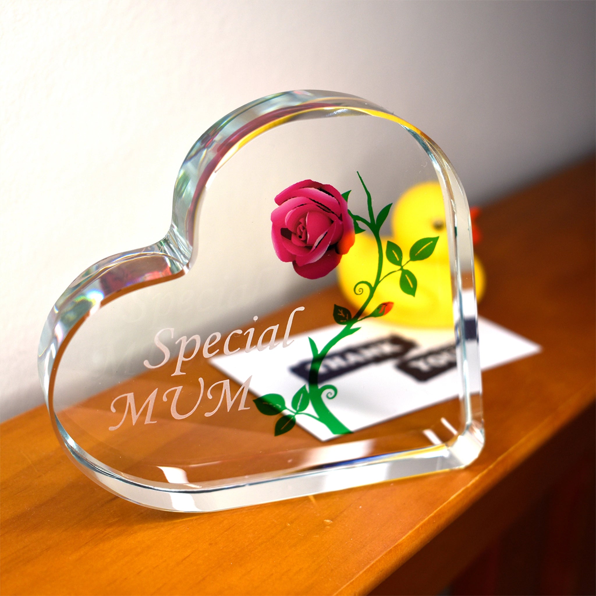 Heart-shaped glass paperweight with a rose and 'Special Mum' engraving on a wooden surface.